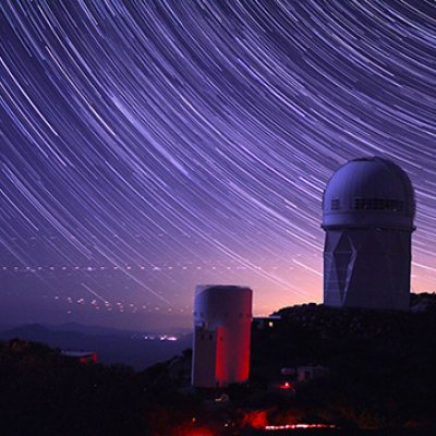 An observatory on a hill under a starry sky. The stars are forming curved lines across the sky.